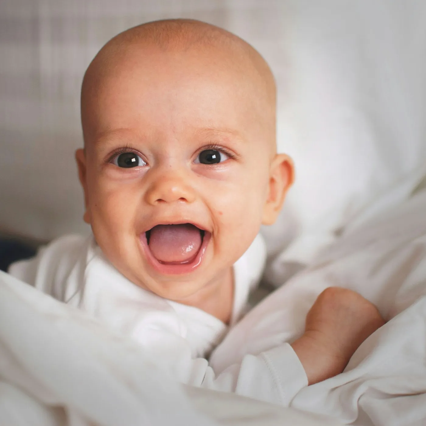 A baby laughing on a white bed