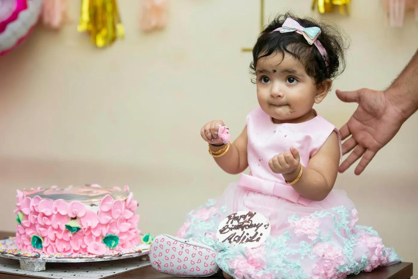 A baby girl at her first birthday, sitting by the cake